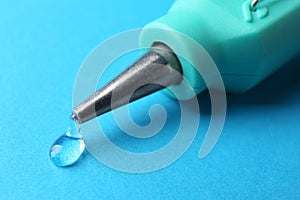 Melted glue dripping out of hot gun nozzle on light blue background, closeup