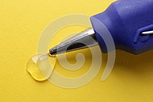Melted glue dripping out of hot gun nozzle on yellow background, closeup
