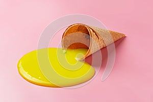 Melted ice cream flows out of a waffle cone on a pink background