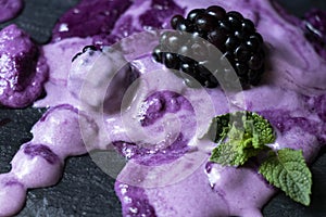 Melted lilac ice cream with blackberries on a black stone board. Stylish, sweet dessert background. And green mint leaves. A