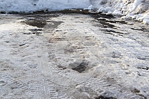 Melted snow on a country road with mud and snow around the edges with tire treads. Puddles on a snowy road in early spring