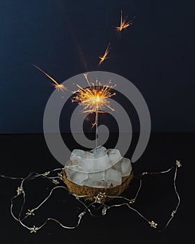 Melting ice in coconut with sparklers on dark background