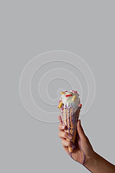 Melting ice cream with pills in a waffle cone in a woman`s hand on a gray background with copy space