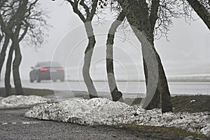 melting snow on the lawn and a car on the road in the fog in a small town in Finland