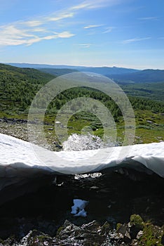 Melting snowfield against the green hills.