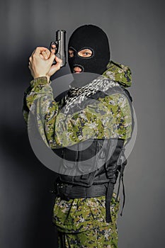 A member of the special police squad, takes aim, holds a pistol. Dressed in a balaclava,  camouflage uniform, bulletproof vest.