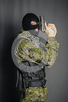 A member of the special police squad, takes aim, holds a pistol. Dressed in a balaclava,  camouflage uniform, bulletproof vest.