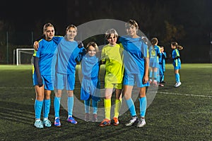 members of school girls football team taking a photo together in a stadium at the evening practice, full shot, team