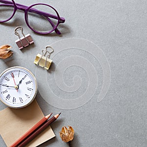 Memo pad, pencil, clock, clip, glasses on gray background