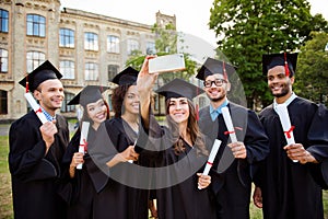 Memories of six international cheerful graduates, posing for shot, attractive brunette lady is taking, wearing gowns and mortar b