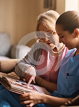 Memory exercises is very important to their health. Shot of a nurse and a senior woman looking at a photo album together