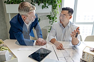 Men architects working on construction plans, engineers discussing on project in office.