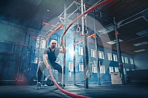 Men with battle rope battle ropes exercise in the fitness gym.