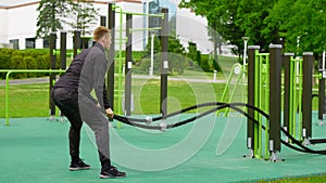 Men with battle rope battle ropes exercise in the street fitness gym.