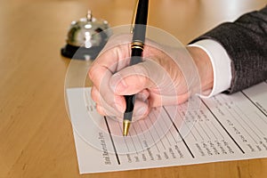 Men business person use pen to writing on a hotel reservation form at reception concierge desk. With a bell ring for guest to call