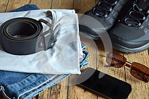 Men casual outfits. Men shoes, clothing and accessories on wooden background - grey t-shirt, blue jeans, sneakers with eyeglass