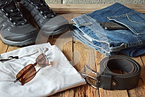 Men casual outfits. Men shoes, clothing and accessories on wooden background - grey t-shirt, blue jeans, sneakers with eyeglass