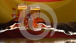 Men clinking beer glasses, Spanish flag on background, sport fans resting in pub