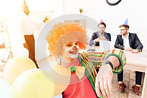 A man in a clown suit and a wig is sitting in the business office on April 1.