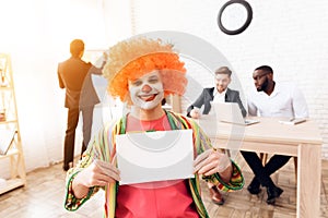 A man in a clown suit and a wig is sitting in the business office on April 1.