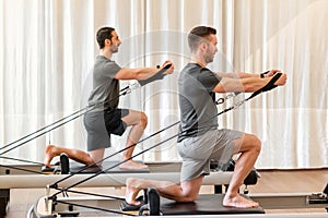 Men doing pilates exercise on reformer bed photo