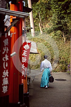 Men dress like Shinto priests, wearing white shirts and green pants. Rear view, walking on a walkway