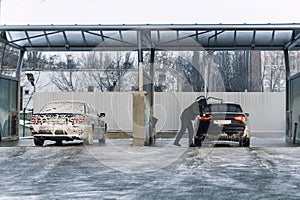 Men driver at car wash with high pressure water equipment pump at self-service outdoor cold snow frosty winter day