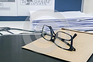 Men eyeglasses on office desk with envelope and tons of business documents piles