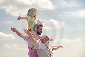 Men generation: grandfather father and grandson playing with raising hands or open arms outdoor on sky. Boy dreams of