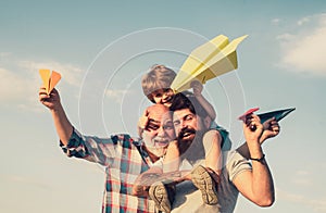 Men generation. Happy grandfather father and grandson with toy paper airplane over blue sky and clouds background