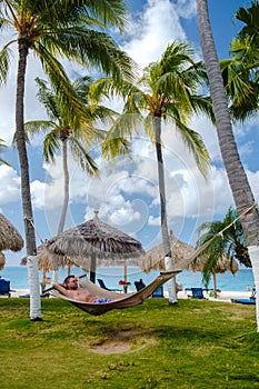 men in a hammock at Palm Beach Aruba Caribbean, white long sandy beach with palm trees Antilles