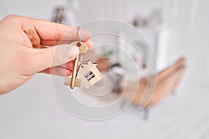 Men hand holding key with house shaped keychain. Modern light lobby interior. Mortgage concept. Real estate, moving home