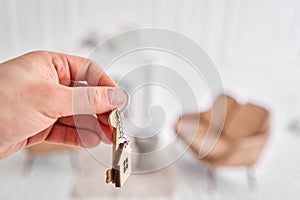 Men hand holding key with house shaped keychain. Modern light lobby interior. Mortgage concept. Real estate, moving home