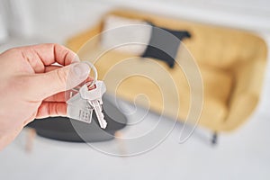 Men hand holding key with house shaped keychain. Modern light lobby interior. Mortgage concept. Real estate, moving home