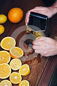 Men Hands barks Lemon Peel for Lemon cake. Many half Cutted Lemons and Citrus on Dark Table. Food and Dessert Preparring. Vertical