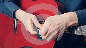 Men hands in blue shirt hold a red guitar and take out pick photo