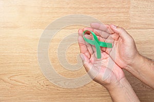Men hands holding kelly bow, green ribbons on wooden background.
