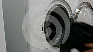 Men hands loads laundry and clothes into washing machine. Large white washing machine in the laundry room.