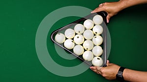 Men hands place pyramid of white balls with help of triangle on billiard table and they are beaten by red ball. Playing