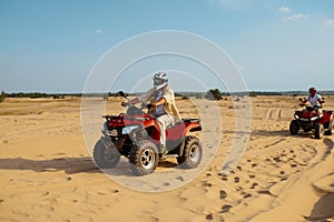 Men in helmets and glasses ride on atv in desert