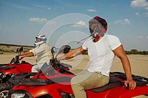 Men in helmets and glasses ride on atv in desert