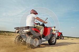 Men in helmets and glasses ride on atv in desert