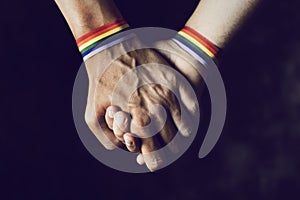 Men holding hands with rainbow-patterned wristband