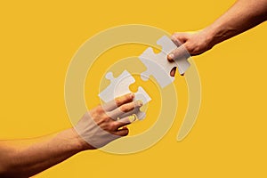 Men holding and putting a piece of jigsaw puzzle together. Two hands trying to connect couple puzzle piece on gray