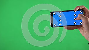 Men holding smartphone horizontally in his hands select and clicks on screen on green background