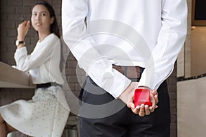 Men holding a wedding band box behind to surprise a girlfriend