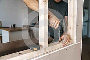 Men in home clothes work with a screwdriver, fixing a wooden frame for a window in their house. Repair yourself