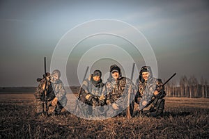 Men hunters group team portrait in rural field posing together against sunrise sky during hunting season. Concept for teamwork