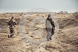 Men hunters running across dry rural field during hunting