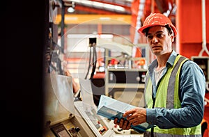 Men industrial engineer wearing a white helmet while standing in a heavy industrial factory behind. The Maintenance looking of